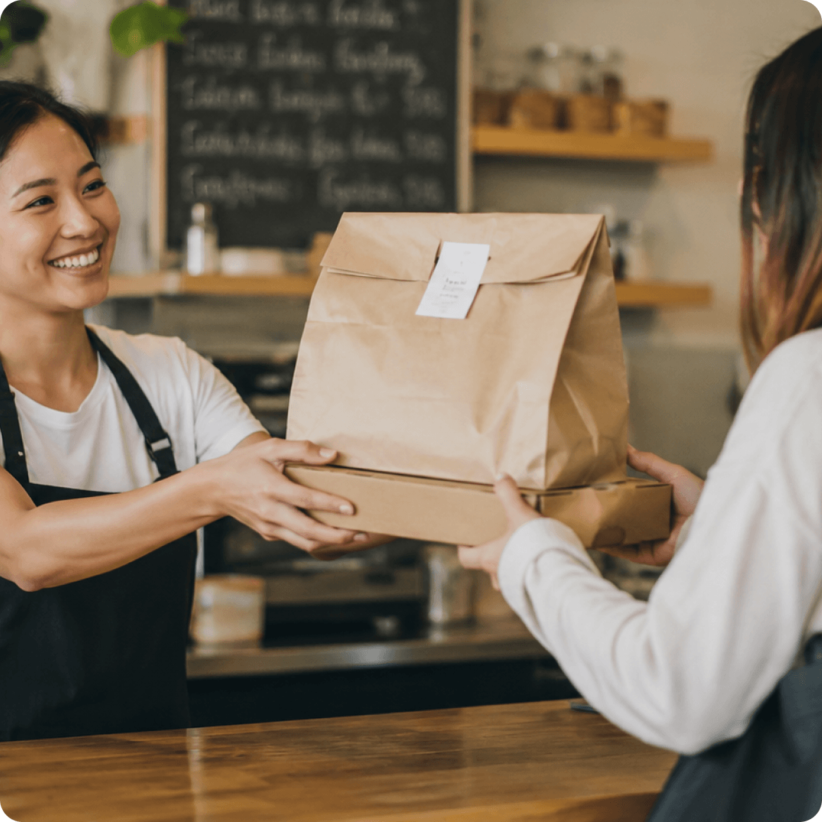 A restaurant team member handing a takeaway order to a customer.