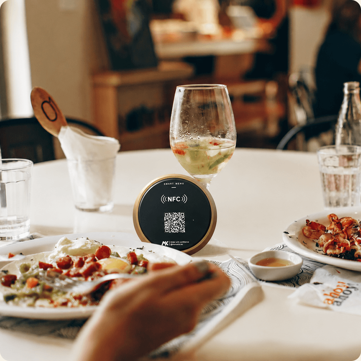 A Menukits NFC card on a restaurant table alongside food and drinks.